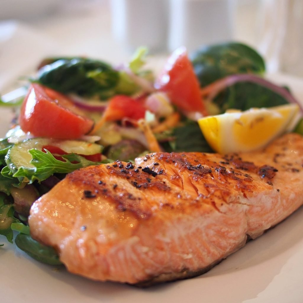 Grilled salmon fillet with fresh salad, tomatoes, and lemon